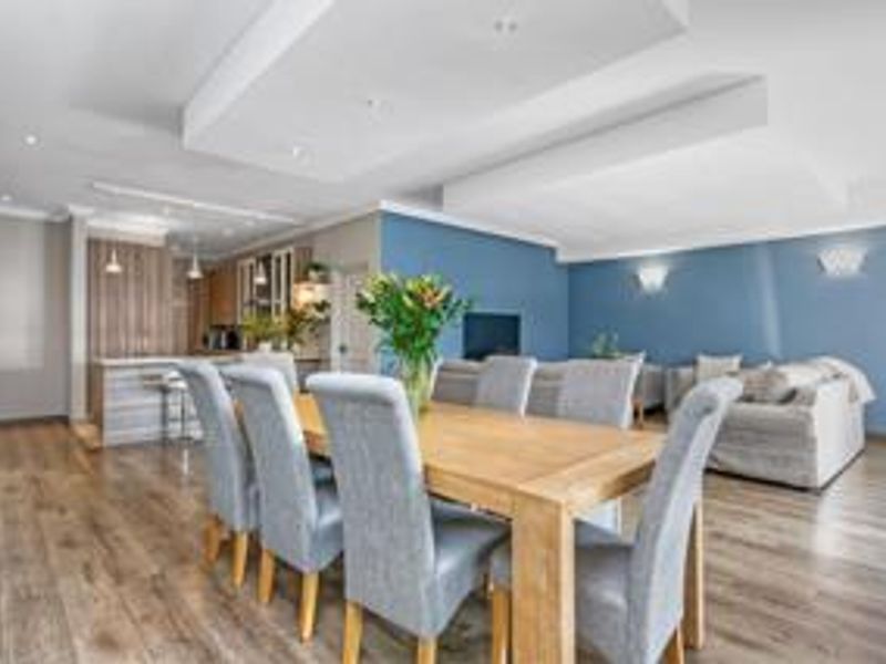 Spacious open-plan living and dining area featuring modern laminate flooring, recessed ceiling details with downlights, and a functional kitchen island.