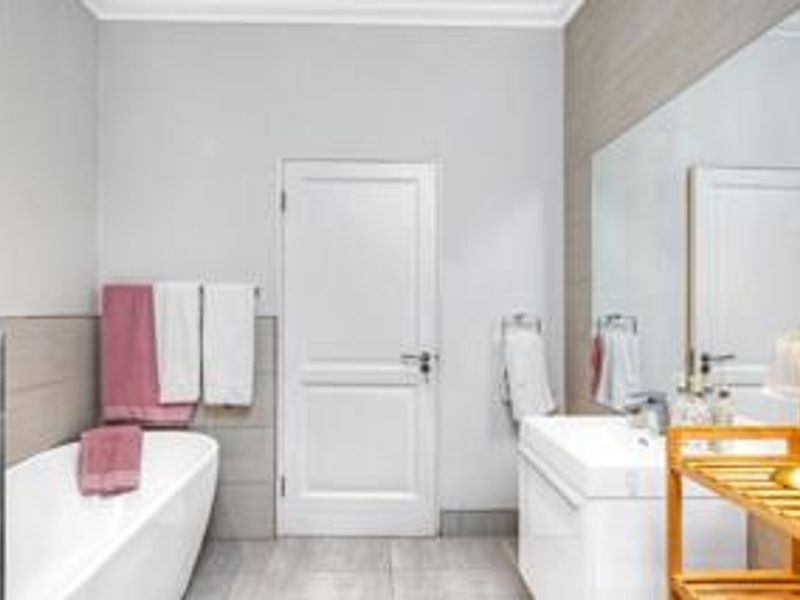 A modern bathroom featuring a freestanding bathtub, a sleek vanity with a basin, and a large wall mirror with neutral tiled finishes.