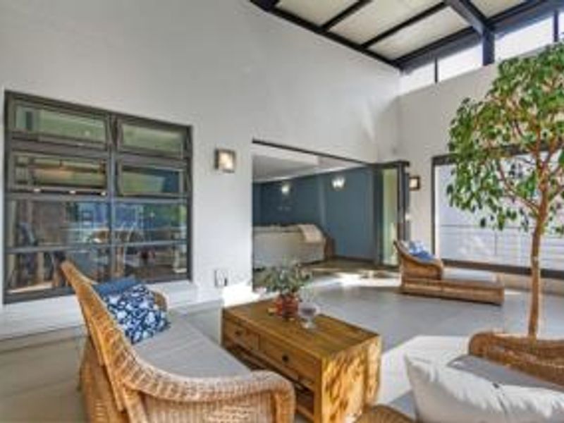 A bright, covered patio area featuring high ceilings with exposed steel beams, tiled flooring, and large windows providing ample natural light.
