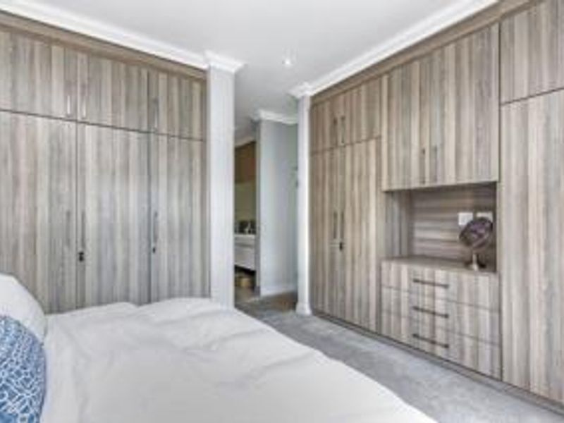 A well-appointed bedroom featuring extensive floor-to-ceiling built-in cabinetry with integrated storage and vanity space, finished in a modern wood-grain laminate.