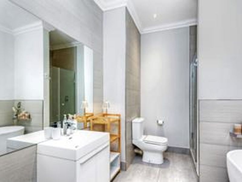 Modern bathroom featuring a sleek vanity, wall-to-wall mirror, contemporary toilet, and a glass-enclosed shower with neutral grey tiling throughout.