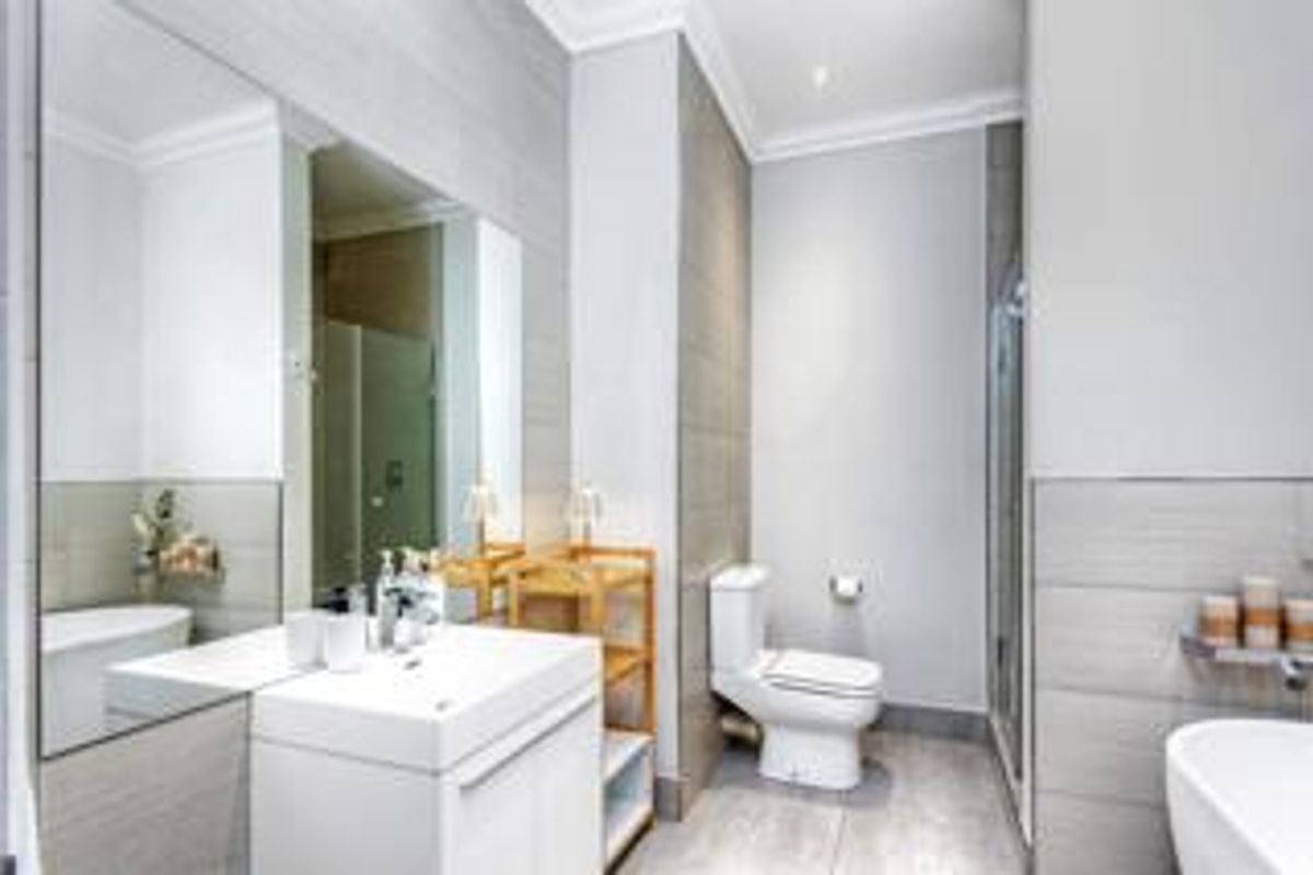Modern bathroom featuring a sleek vanity, wall-to-wall mirror, contemporary toilet, and a glass-enclosed shower with neutral grey tiling throughout.
