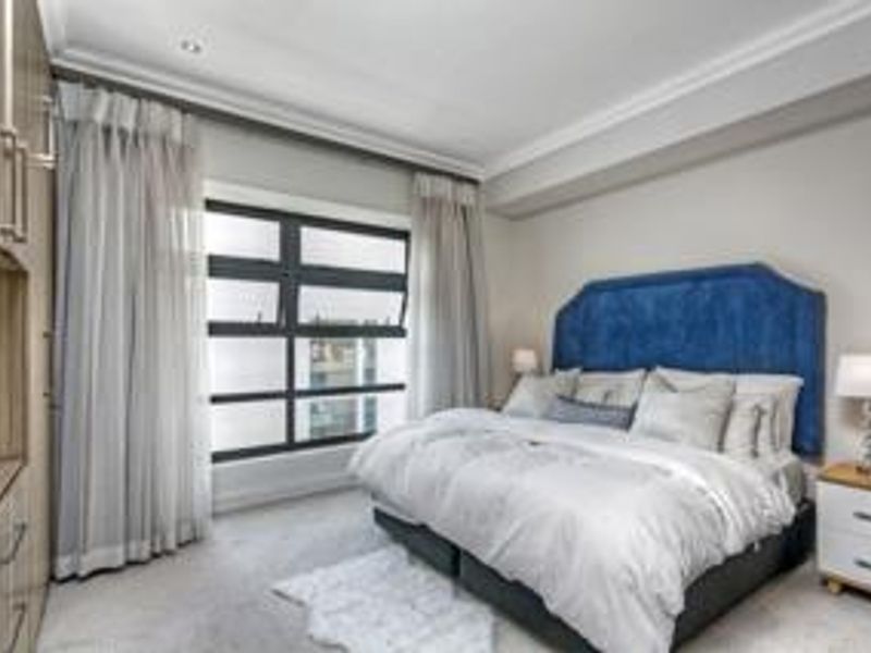 A well-maintained bedroom featuring built-in cupboards, elegant cornicing, recessed lighting, and large windows that provide ample natural light.