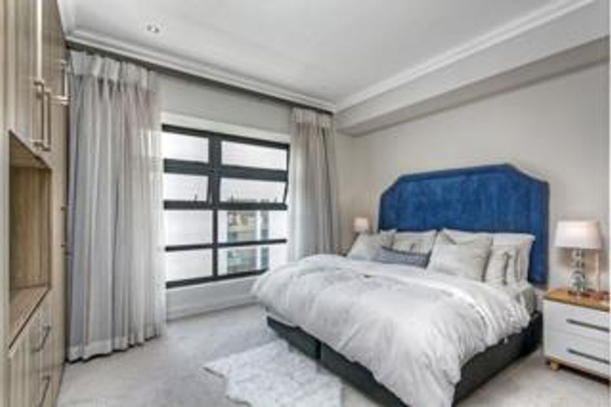 A well-maintained bedroom featuring built-in cupboards, elegant cornicing, recessed lighting, and large windows that provide ample natural light.