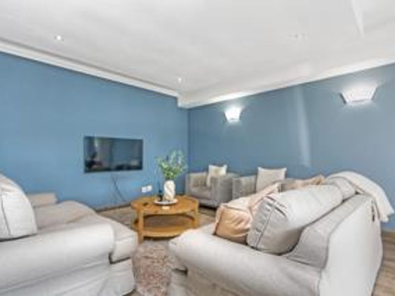 A well-maintained living room featuring blue accent walls, recessed ceiling lighting, wall-mounted sconces, and durable laminate flooring.
