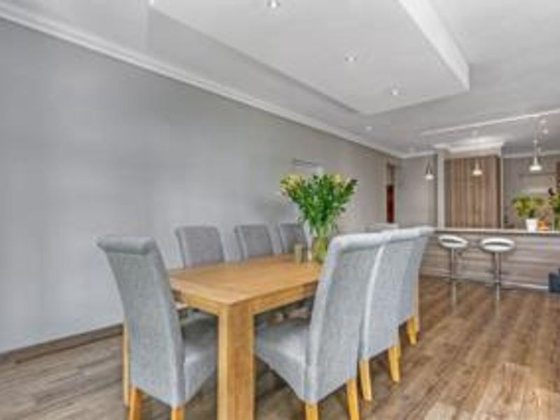 Open plan living and dining area featuring modern laminate flooring, a recessed ceiling with downlights, and a functional kitchen island with built-in cabinetry.