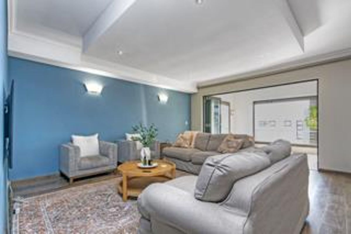 A spacious living room featuring a recessed ceiling, wall sconces, and laminate flooring, with large sliding glass doors leading to an outdoor area.