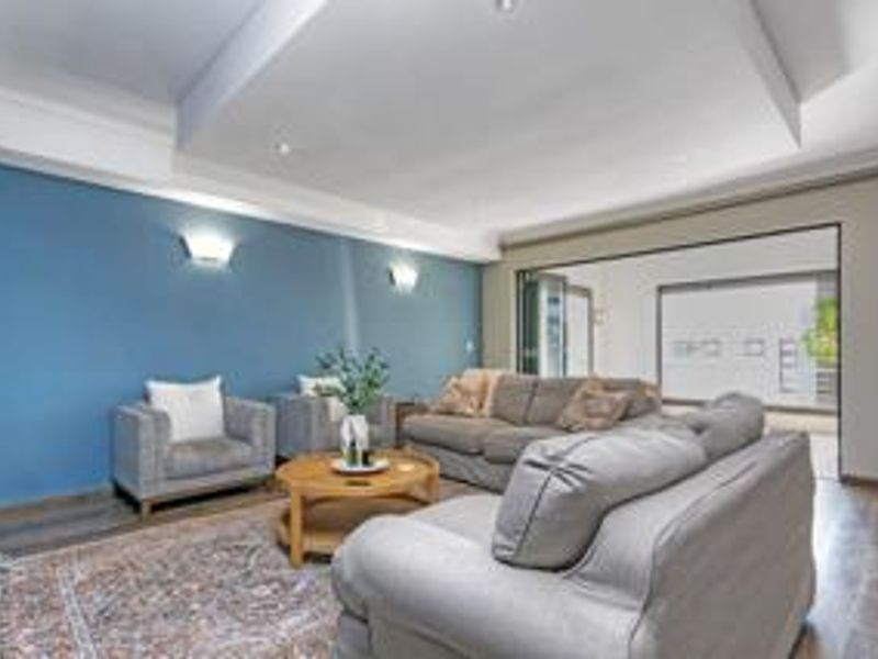 A spacious living room featuring a recessed ceiling, wall sconces, and laminate flooring, with large sliding glass doors leading to an outdoor area.