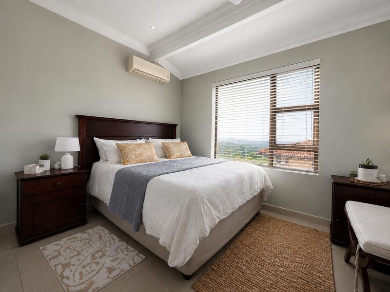 A well-maintained bedroom featuring neutral wall tones, crown molding, tiled flooring, an integrated air conditioning unit, and large windows with venetian blinds.