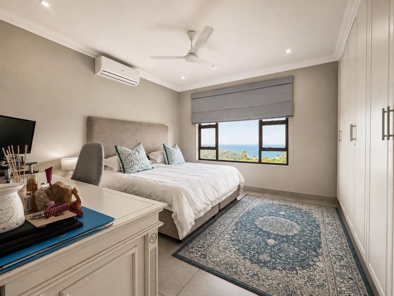 A well-maintained bedroom featuring built-in cupboards, a ceiling fan, air conditioning, and large windows offering scenic ocean views.