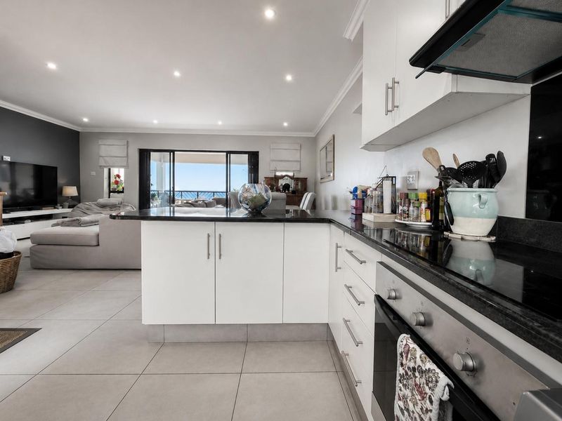 Modern open-plan kitchen and living area featuring sleek white cabinetry, granite countertops, integrated appliances, and large sliding doors leading to a balcony.