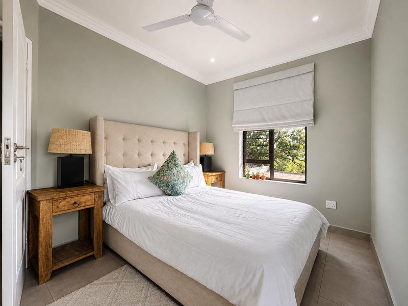 A well-maintained bedroom featuring neutral wall tones, tiled flooring, crown molding, a ceiling fan, and a window with a fitted roman blind.