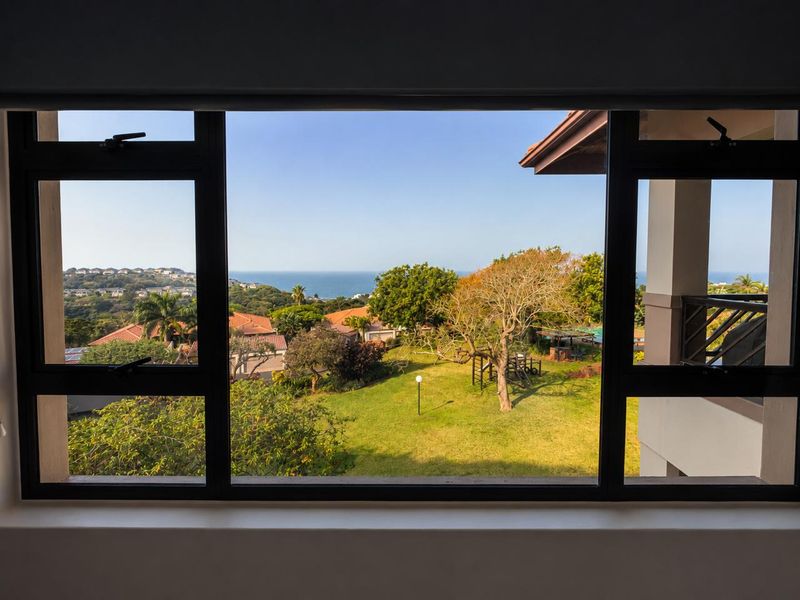 A scenic view of the surrounding estate and distant ocean captured through a modern aluminium-framed window.