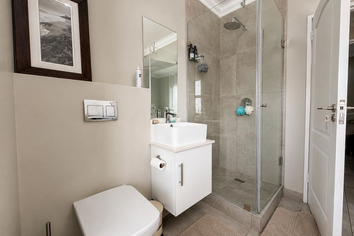 Modern bathroom featuring a wall-mounted toilet with concealed cistern, a compact vanity with vessel sink, and a glass-enclosed shower with rain shower head.