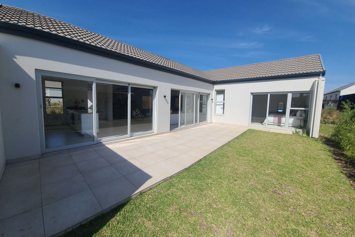 Rear view of the cluster home featuring a spacious tiled patio, large sliding glass doors, and a well-maintained garden area.