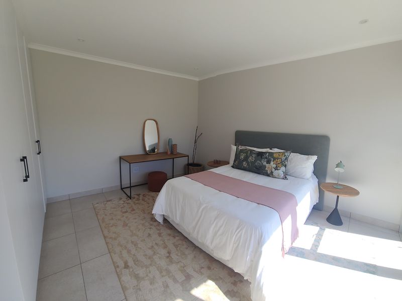 A bright and modern bedroom featuring neutral walls, tiled flooring, built-in cupboards, and a sliding glass door providing natural light.