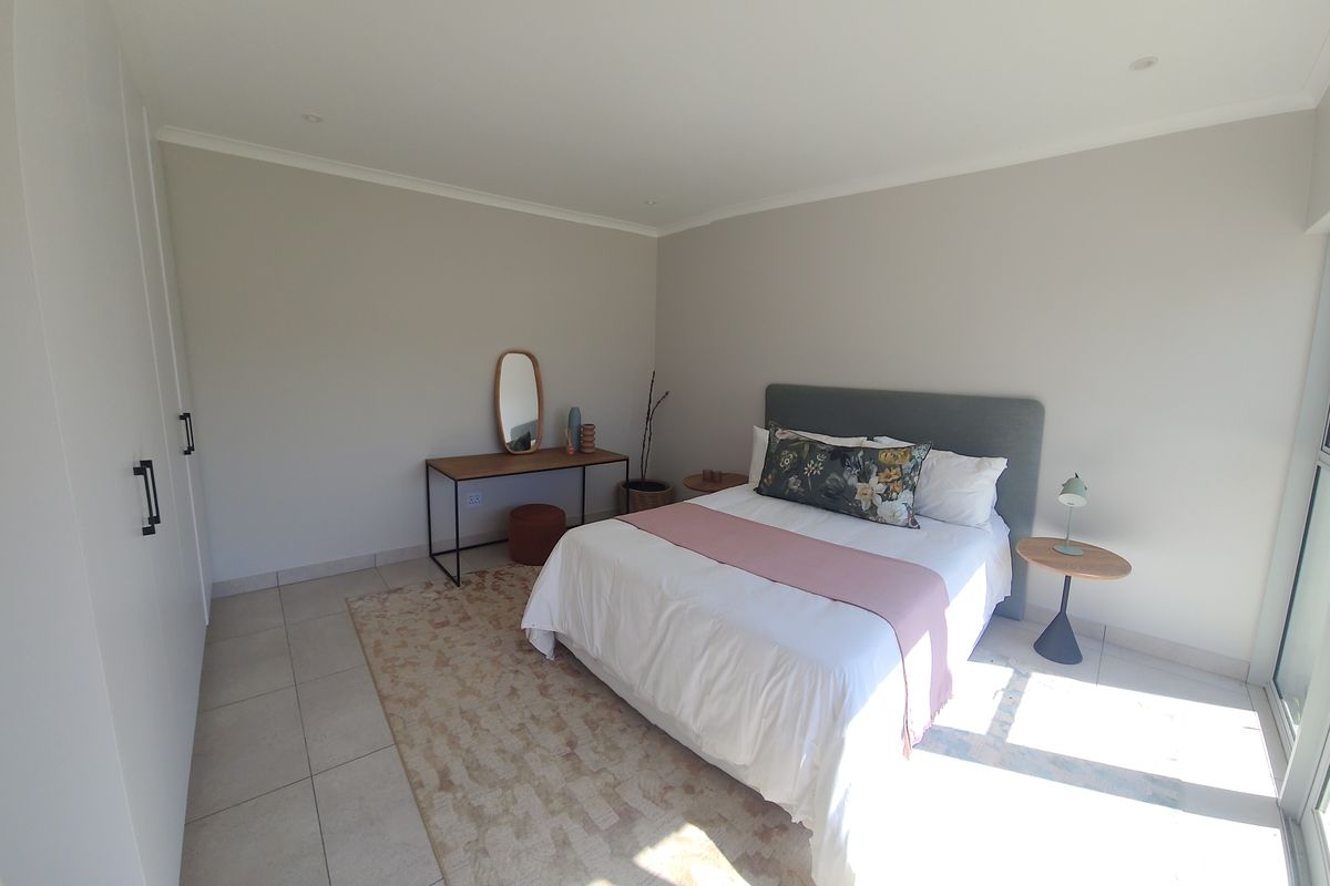 A bright and modern bedroom featuring neutral walls, tiled flooring, built-in cupboards, and a sliding glass door providing natural light.