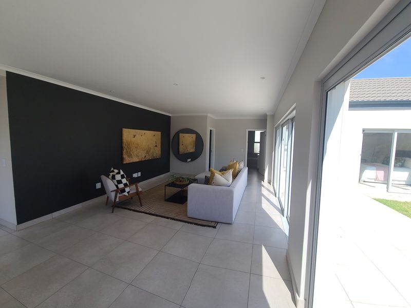 Spacious living room featuring large format floor tiles, a dark accent wall, and expansive sliding glass doors providing seamless access to the outdoor area.