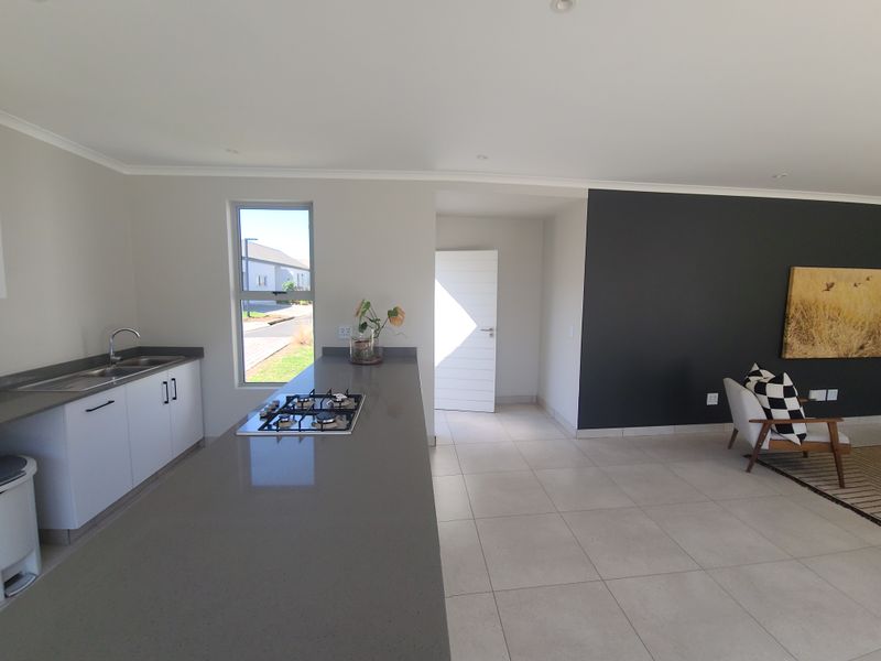 Modern open-plan kitchen and living area featuring sleek quartz countertops, a gas hob, and neutral tiled flooring with a contemporary dark feature wall.