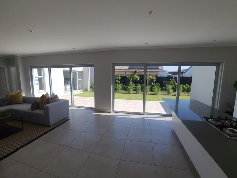 Spacious open-plan living area featuring a modern kitchen island with a gas hob, large sliding doors, and seamless access to the outdoor patio and garden.