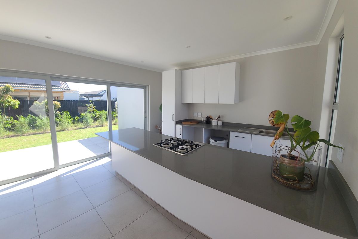 Modern kitchen featuring a central island with a gas hob, stone countertops, ample cabinetry, and large sliding doors opening to the garden.