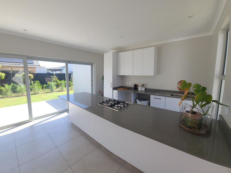 Modern kitchen featuring a central island with a gas hob, stone countertops, ample cabinetry, and large sliding doors opening to the garden.