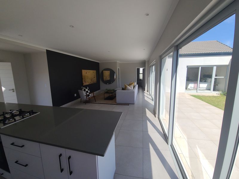 Modern open-plan living area featuring a sleek kitchen island with gas hob, large format floor tiles, and expansive sliding doors opening to a patio.