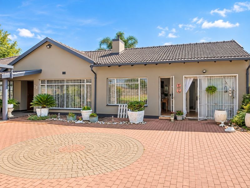 Front elevation of a well-maintained house featuring a paved circular driveway, tiled roof, and secure entrance with security gates and bars.