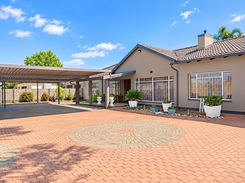 Front elevation of a well-maintained house featuring a large paved driveway, a spacious carport, and secure window treatments.