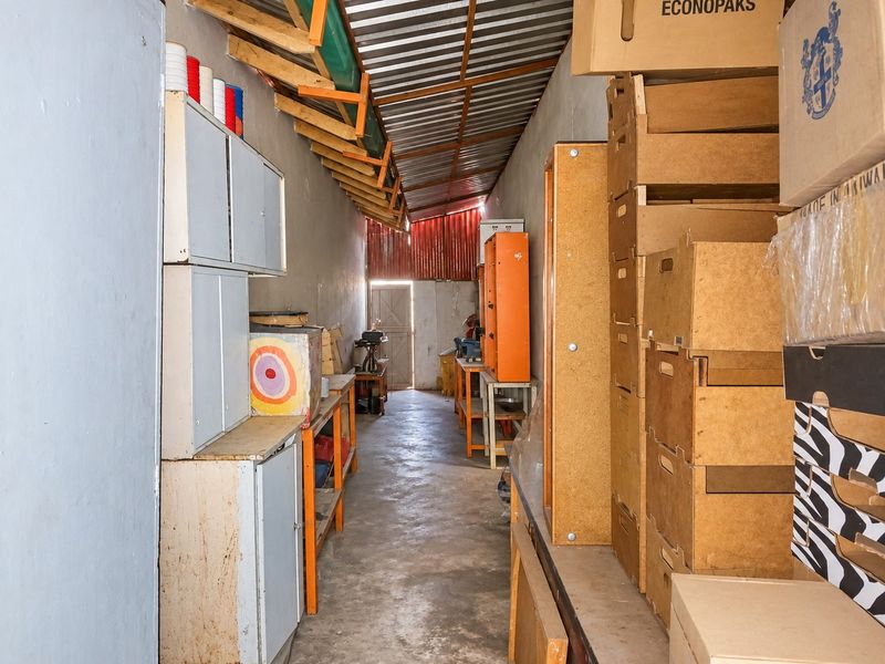 A functional utility or storage space featuring concrete flooring, built-in cabinetry, and exposed timber rafters under a corrugated metal roof.