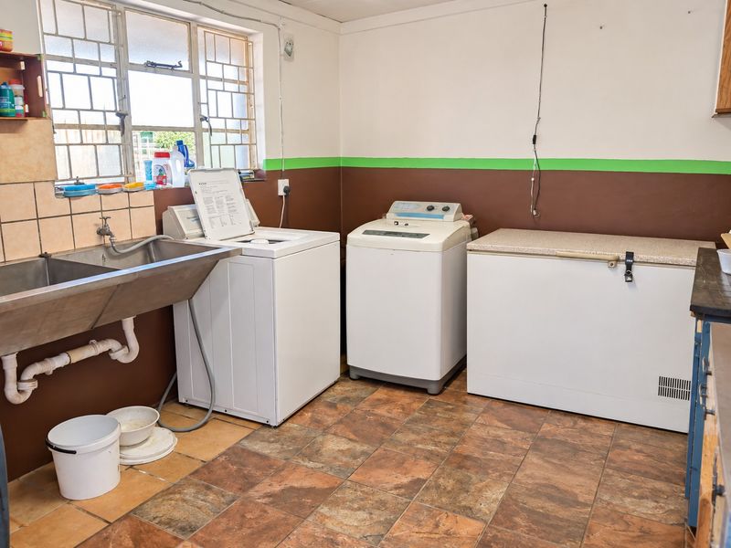 Functional laundry room featuring a stainless steel utility sink, tiled splashback, and ceramic floor tiles, providing a practical space for household chores.