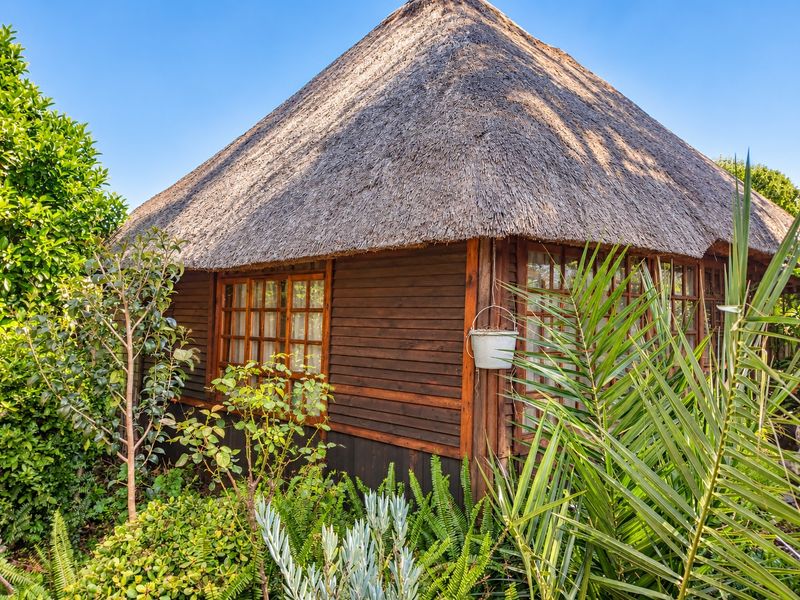 A charming timber-clad structure featuring a traditional thatched roof and timber-framed windows, set within a lush, well-maintained garden environment.