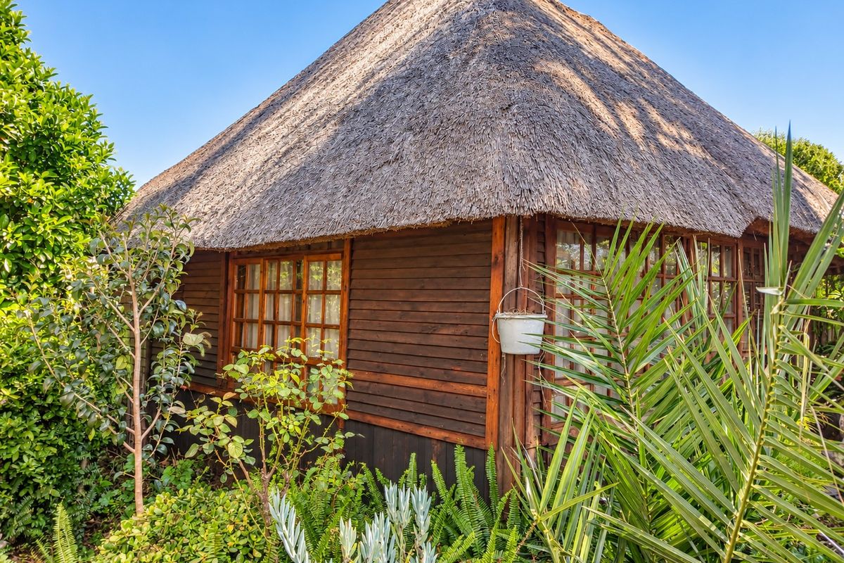 A charming timber-clad structure featuring a traditional thatched roof and timber-framed windows, set within a lush, well-maintained garden environment.