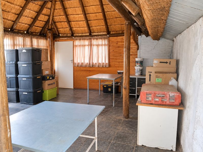 A rustic utility space featuring a traditional thatched roof, timber wall paneling, and tiled flooring, suitable for a workshop or storage area.