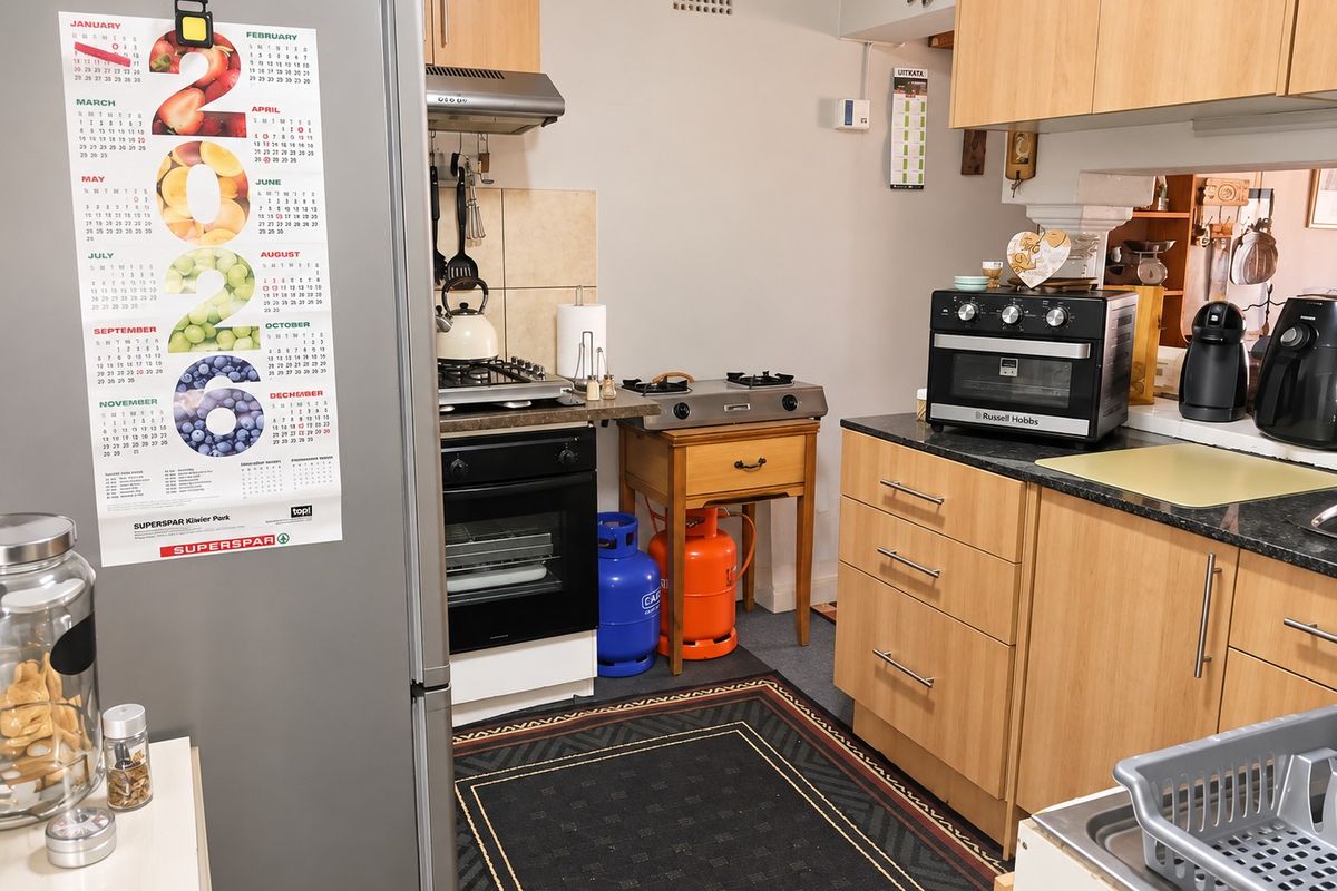 A functional kitchen featuring light wood cabinetry, granite countertops, a built-in oven, and a gas hob with an extractor fan.