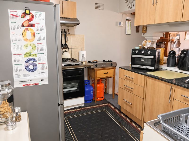 A functional kitchen featuring light wood cabinetry, granite countertops, a built-in oven, and a gas hob with an extractor fan.