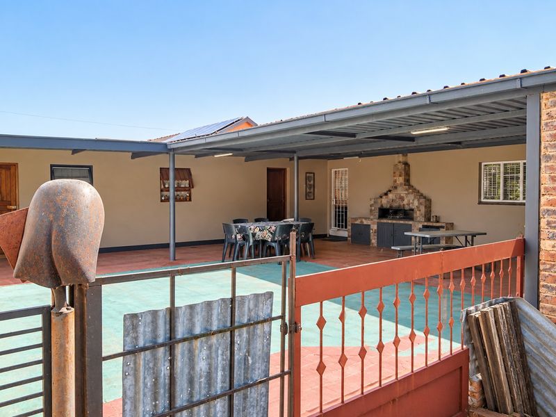 A spacious covered outdoor patio featuring a built-in brick braai, tiled flooring, and a metal roof structure, ideal for outdoor entertaining.