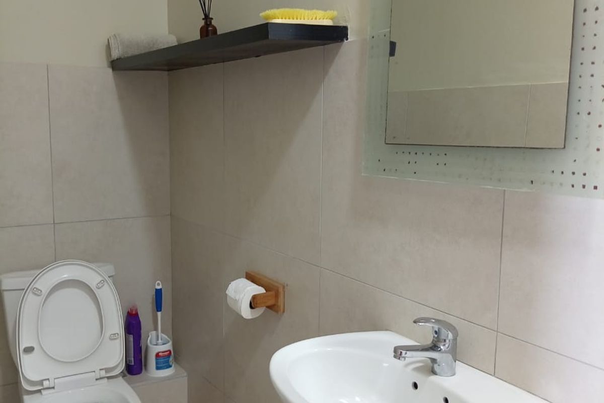 A clean and functional bathroom featuring a pedestal basin, chrome mixer tap, toilet, and neutral ceramic wall and floor tiling.