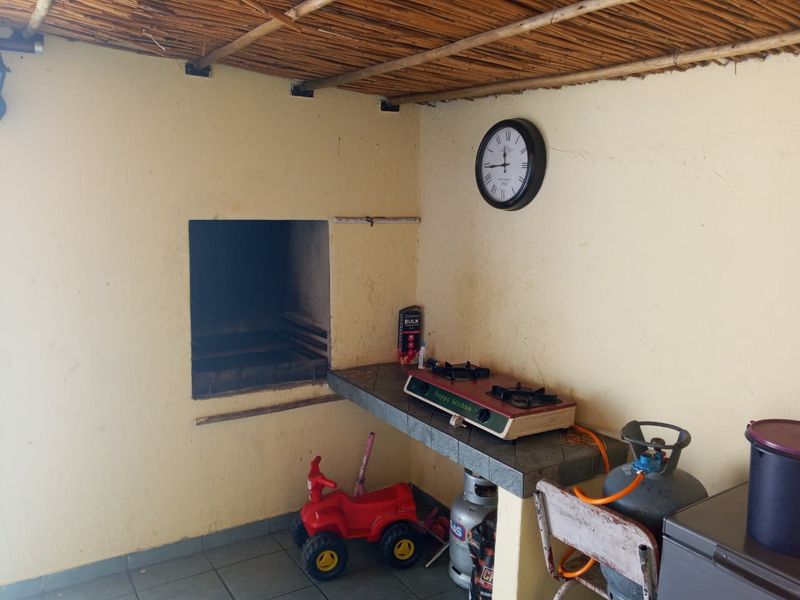 Covered outdoor patio area featuring a built-in braai, tiled prep counter, and rustic thatched roofing, suitable for outdoor entertaining.