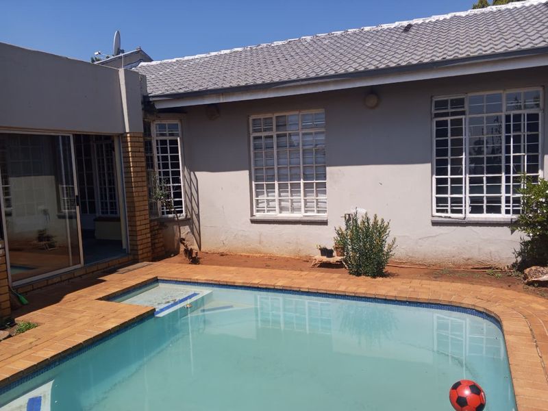 Rear exterior view featuring a swimming pool with brick coping, adjacent to the main dwelling with sliding glass doors and security-barred windows.