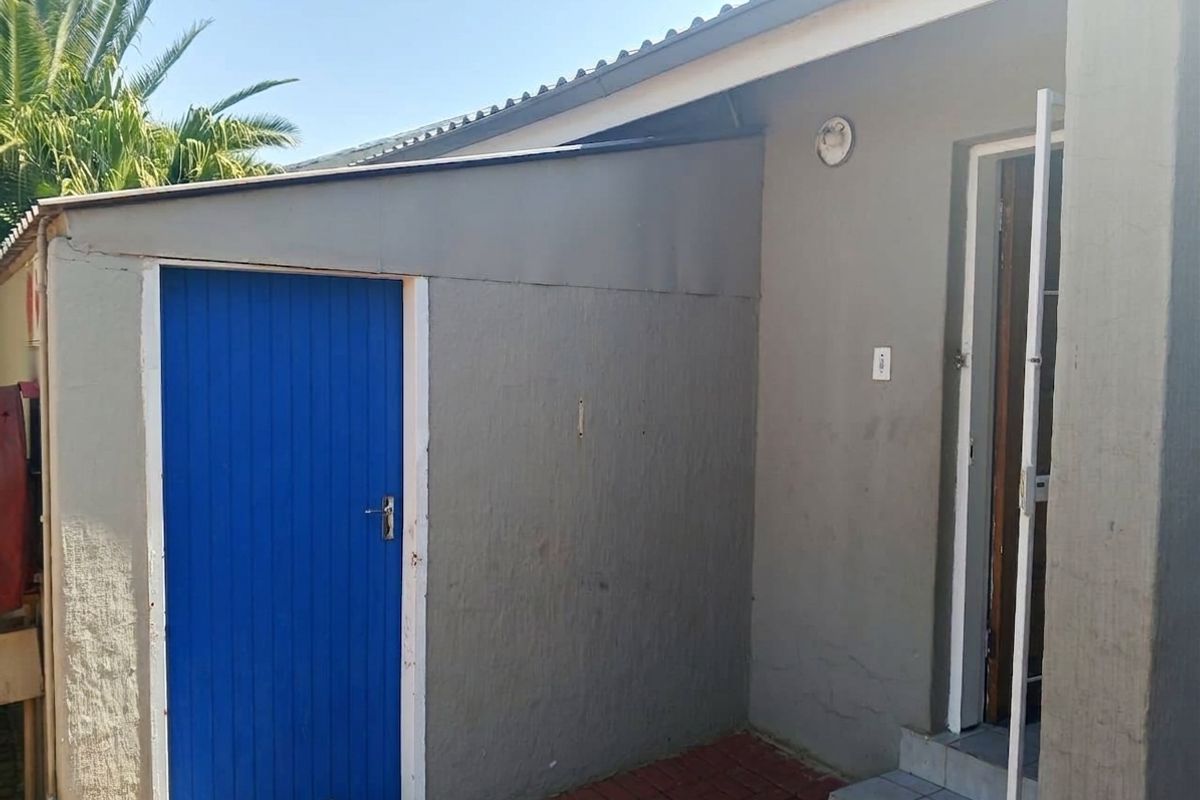 Rear exterior view of the townhouse featuring a paved area, painted exterior walls, and access doors.