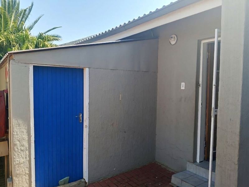 Rear exterior view of the townhouse featuring a paved area, painted exterior walls, and access doors.