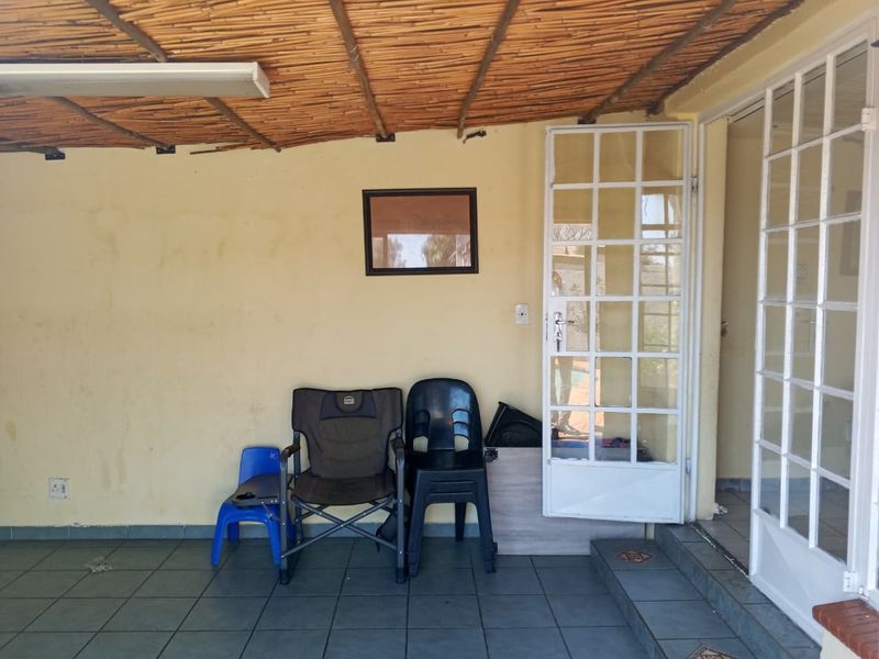 Covered patio area featuring tiled flooring and a thatched roof structure, providing direct access to the interior through white-framed french doors.