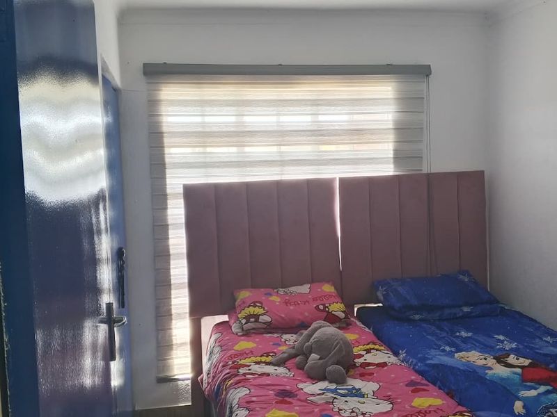 A compact bedroom featuring tiled flooring, a modern roller blind, and a central ceiling light fixture.