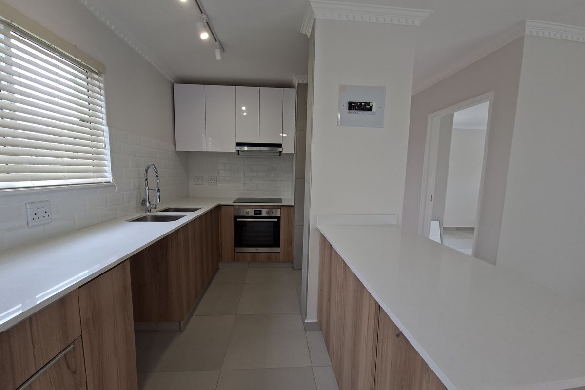 Modern kitchen featuring sleek wood-finish cabinetry, white quartz countertops, subway tile backsplash, and integrated stainless steel appliances.