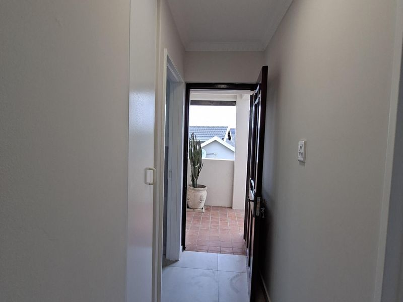 A clean, neutral hallway featuring tiled flooring, a built-in cupboard, and a doorway leading to an outdoor balcony area.
