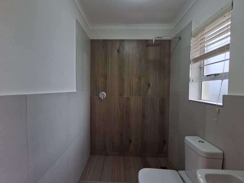 Modern bathroom featuring a walk-in shower with wood-look tiling, a rain shower head, pedestal basin, and dual-flush toilet.
