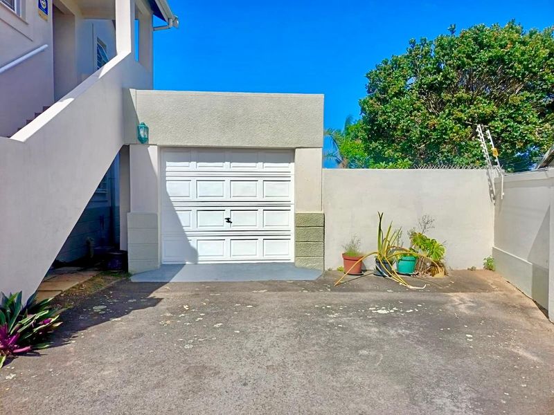 A single garage unit with a white sectional door, concrete driveway, and adjacent exterior staircase.