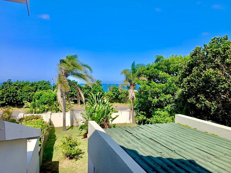 Elevated view overlooking a landscaped garden, perimeter wall, and distant ocean horizon under a clear blue sky.