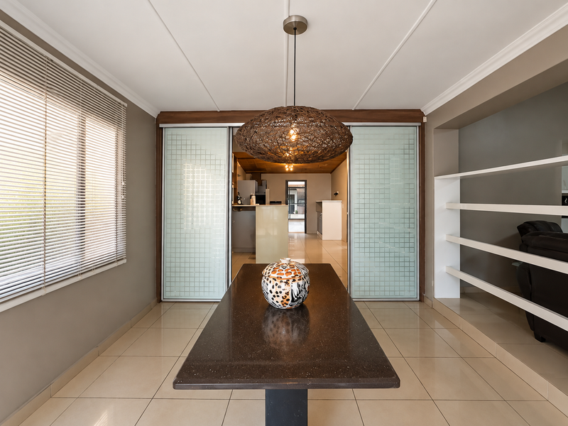Dining room featuring tiled flooring, built-in shelving, and sliding glass doors leading to the kitchen area, illuminated by a decorative pendant light.